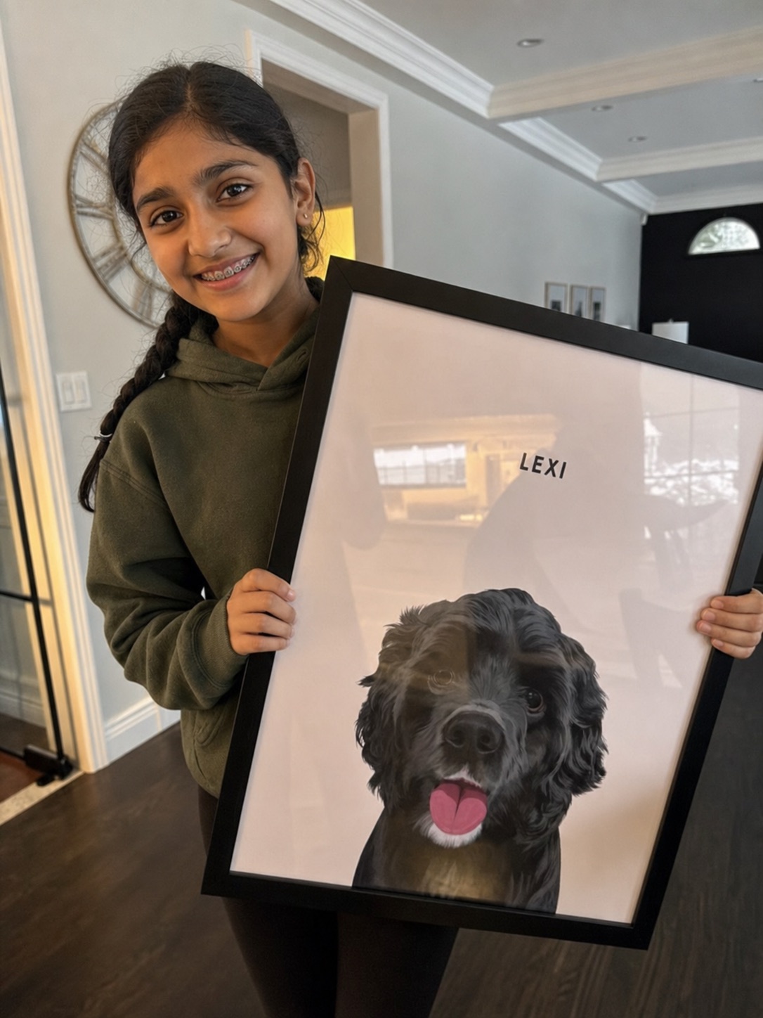Young Indian girl with braces smiling as she holds a large framed portrait of her black dog Lexi
