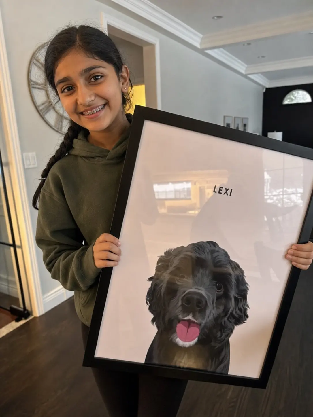 Young Indian girl with braces smiling as she holds a large framed portrait of her black dog Lexi